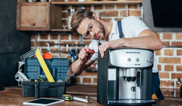 professional young repairman in eyeglasses fixing coffee machine